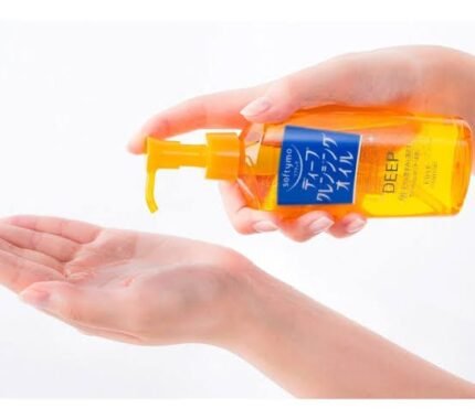 Hand holding a yellow bottle of Softymo Deep Cleansing Oil and dispensing oil into the palm of another hand.