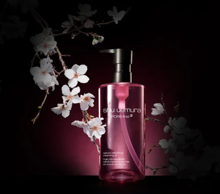 Elegant product shot of Shu Uemura Pore Finist 2 Sakura Refreshing Cleansing Oil bottle against a dark background with white cherry blossoms.