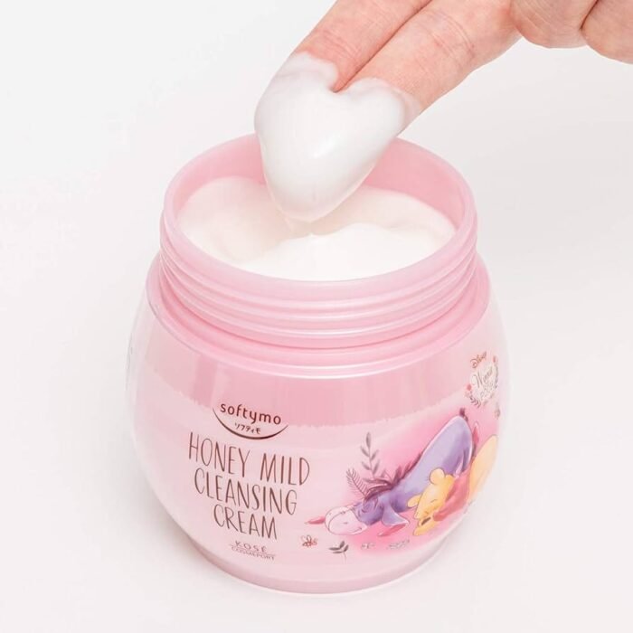 Fingers scooping white cleansing cream from a pink jar of Softymo Honey Mild Cleansing Cream featuring Winnie the Pooh.