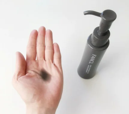 A hand with black makeup is being cleaned with FANCL Mild Cleansing Oil - Black & Smooth, with the product bottle visible.