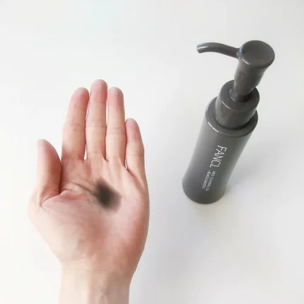 A hand with black makeup is being cleaned with FANCL Mild Cleansing Oil - Black & Smooth, with the product bottle visible.