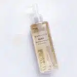 Clear bottle of Muji Sensitive Skin Cleansing Oil with a pump, shown next to a drop of the oil on a white surface.